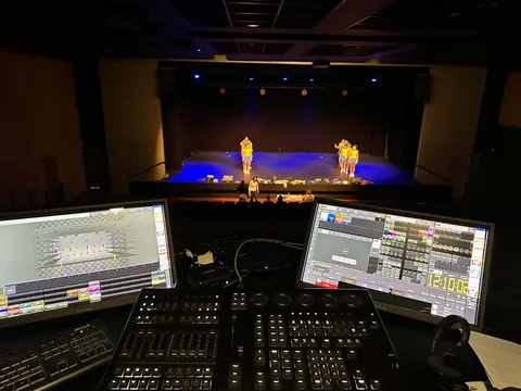 Régie lumière avec deux écrans et console face aux artistes sur scène